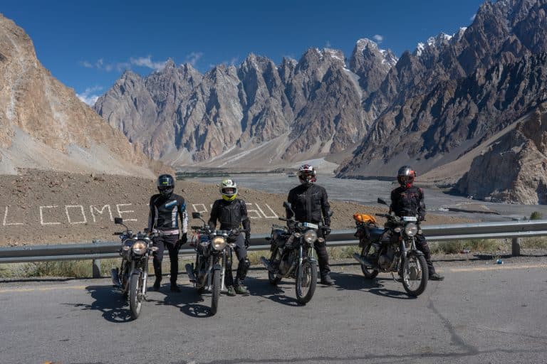 group of ADV Outriders pose by vast mountain range while on motorbike tour in Pakistan