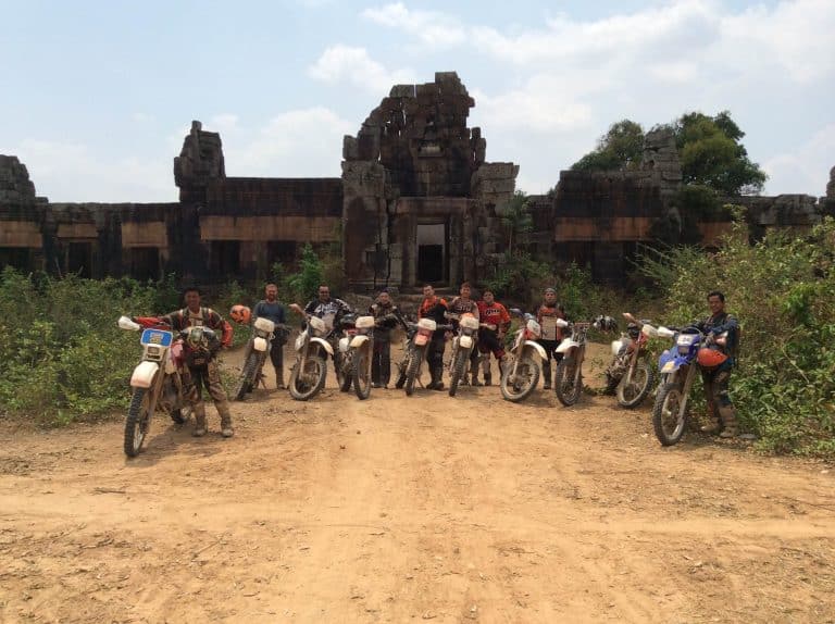 team of riders stopped outside of temple ruins in the Cambodian jungle